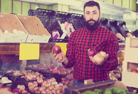 Adult man seller showing onions in grocery shopの写真素材