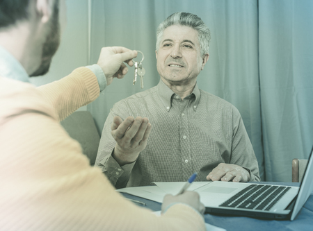 Adult man and agent sign contract of rent apartments and hand over keysの写真素材