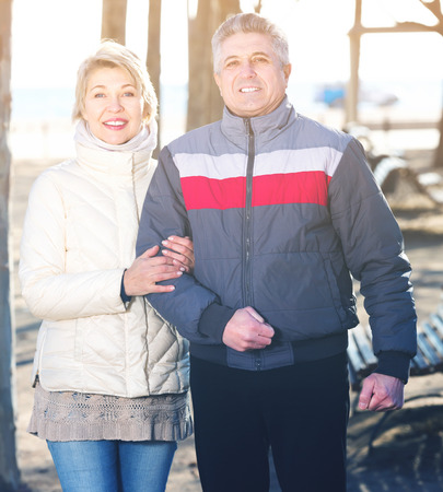 Glad husband and wife spend day together walking in park on seashoreの写真素材