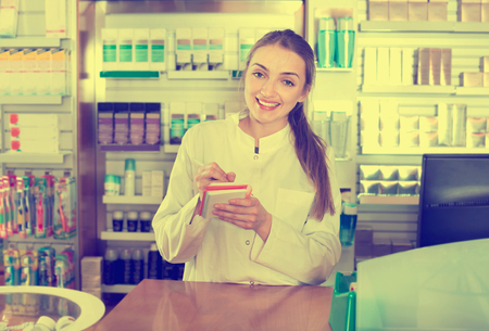 Smiling cheerful young female pharmacist posing in drugstoreの写真素材