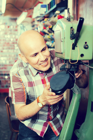 Smiling mature workman  stitching footwear on machine in shoe atelierの写真素材