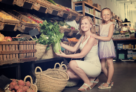 Glad positive  mother with pretty smiling daughter shopping various veggies in food storeの写真素材