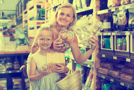 Glad female customer with daughter choosing different cookies and crisp bread in the food shop. Focus on childの写真素材