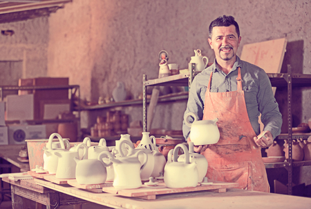 Smiling male sculptor having ceramics in hands and standing in workroomの写真素材