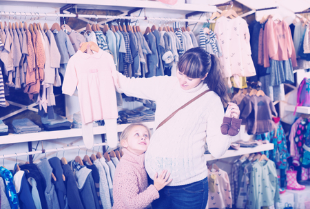 Pregnant woman and her daughter decided to purchase sliders and dresses in the shop of children's clothesの写真素材