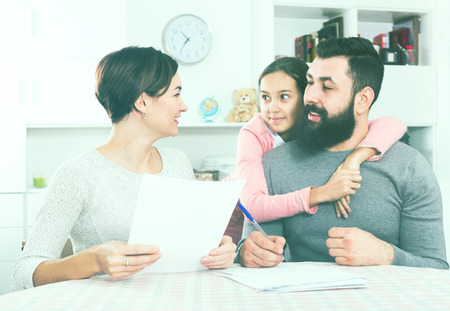 Young father and mother signing realty papers with their daughterの写真素材