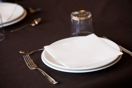 Dining set of empty white plate, knife, fork and glass on the table in the restaurantの写真素材