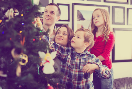 Happy family putting decorations on Christmas tree at homeの写真素材