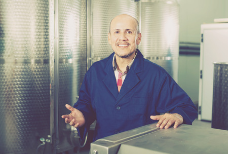 Cheerful mature man in uniform working in wine secondary fermentation sectionの写真素材