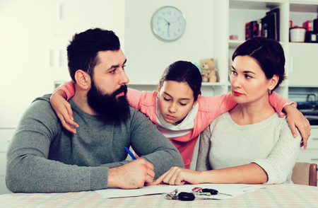Young sad parents signing papers for divorce while their daughter at home interiorの写真素材