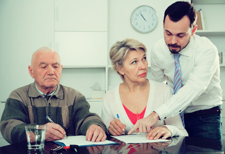 Father and mature daughter with bank employee signing loan agreementの写真素材