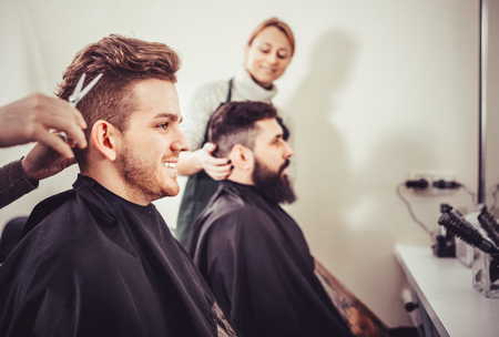 Positive smiling efficient clients having their hair cut by hairdressers at salonの写真素材
