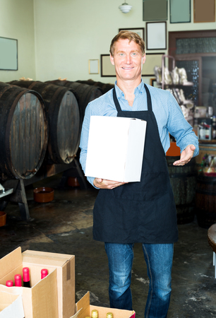 Portrait of happy male worker wearing uniform with big package in hands in wineryの写真素材