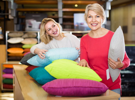 Young girl and aged mother choosing pillows in home textile shopの写真素材