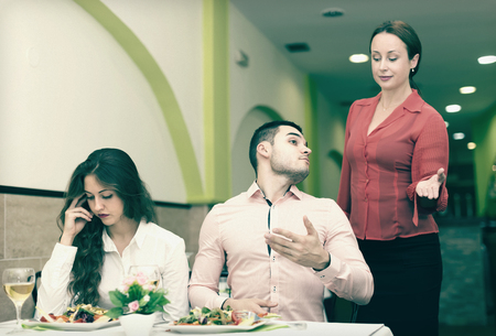 Wife caught husband with young mistress having dinner in cafe. Focus on manの写真素材