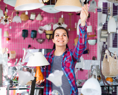 Smiling happy positive girl in lighter shop chooses stylish and modern chandelier lampの写真素材