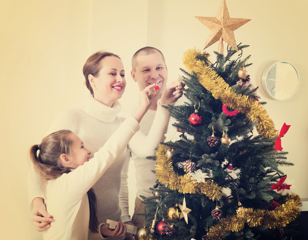 Laughing family of three preparing for Christmas in living room. Focus on womanの写真素材