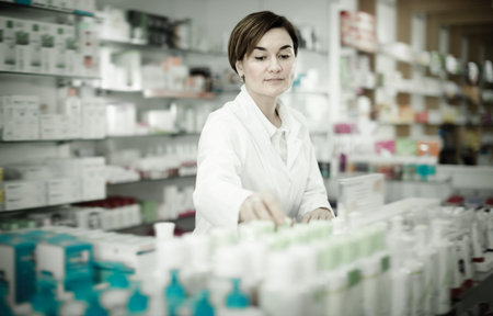 Cheerful female pharmacist arranging assortment of products in pharmacyの写真素材