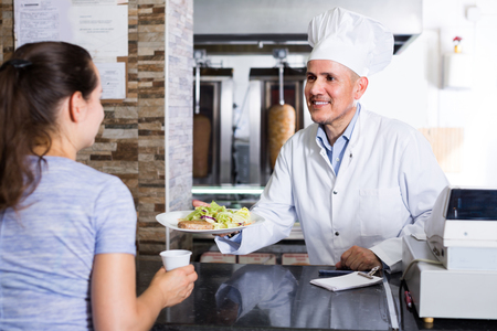 smiling mature man chef in uniform giving order with kebab plate to customerの写真素材