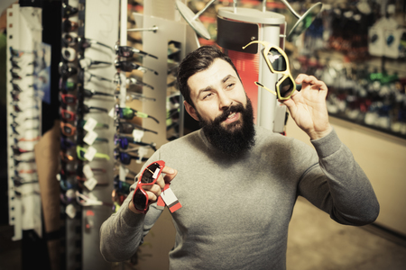 Cheerful guy deciding on new sunglasses in sports equipment storeの写真素材