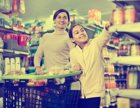 Young woman customer with girl looking for food supplies in a supermarket. Focus on childの写真素材