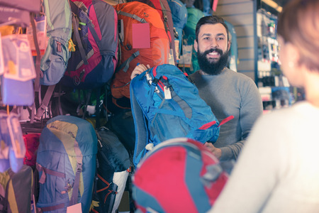 young pair examining various rucksacks in sports equipment storeの写真素材