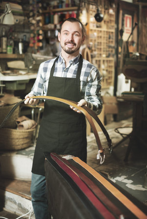 Positive young male worker demonstrating assortment in leather workshop
