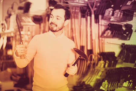 Young smiling cheerful man choosing various tools in garden equipment shopの写真素材
