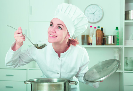 Young female cook tasting food while preparing in kitchenの写真素材