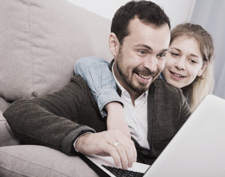 Young father and teenage daughter booking hotel online at homeの写真素材