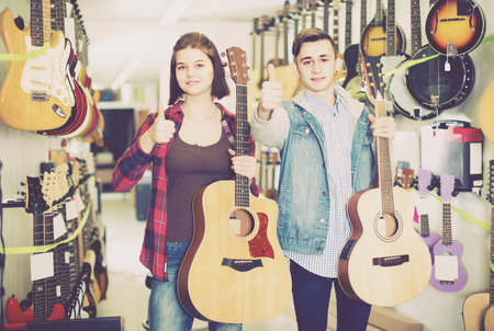Smiling teenage customers deciding on suitable acoustic guitar in guitar shop