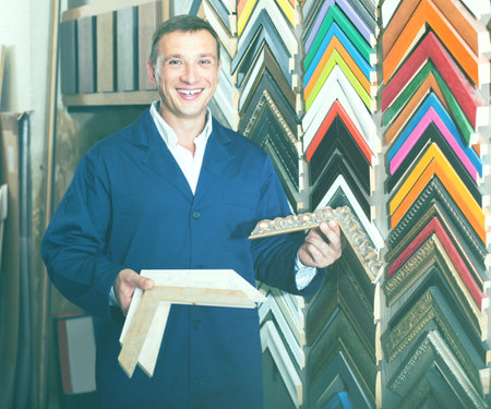 portrait of happy european man in uniform choosing framing moulding in studio