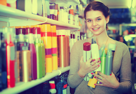 Young female shop assistant is demonstrating hair care product in cosmetics shop.の写真素材