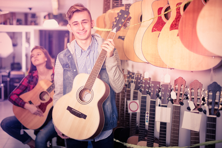 Happy teenage boy and girl choosing best acoustic guitar in guitar shopの写真素材
