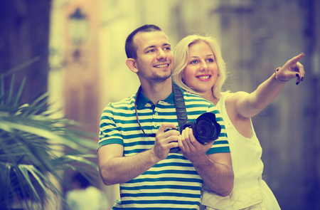 Happy man and woman tourists taking camera in hands and photographing in cityの写真素材
