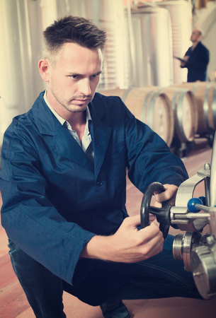 young man machinery operator working in secondary fermenting section on wineryの写真素材