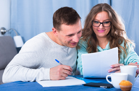 Middle-aged couple signing beneficial financial agreement together at homeの写真素材
