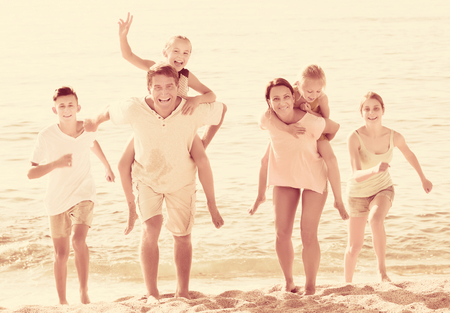 Smiling young parents with four children in different ages sitting on parents back taking walk on beachの写真素材