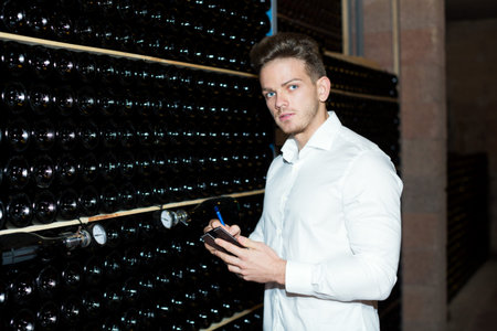 Glad male worker checking secondary fermentation of wine at sparkling wine factory