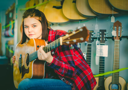 Teen girl examining various acoustic guitars in guitar shop
