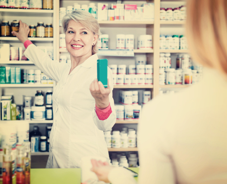 Positive smiling mature female seller suggesting care products to young customer in specialized shopの写真素材