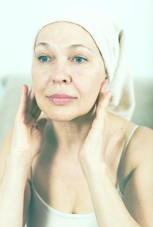 Senior woman putting cream on face during beauty procedures at homeの写真素材