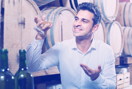 smiling adult man having glass with brandy in winery storeの写真素材