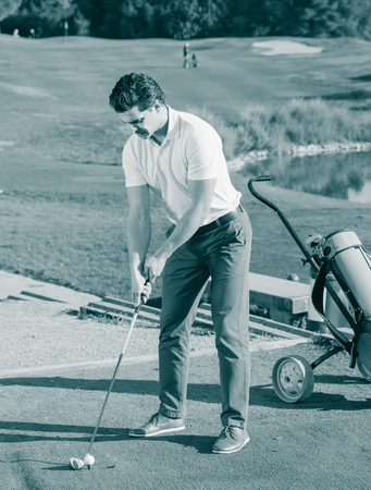 positive american man playing golf is going to hit ball at golf courseの写真素材