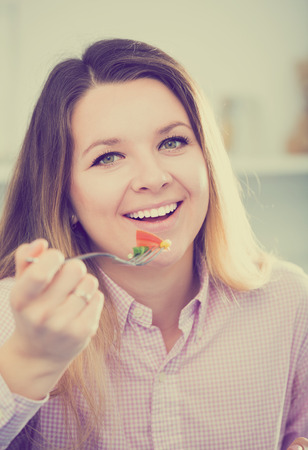 Young attractive girl eating green salad with pleasure at homeの写真素材