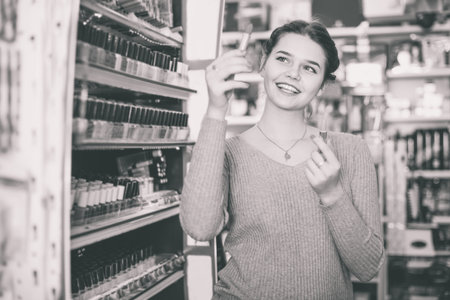 Happy cheerful positive woman customer browsing rows of lipstick in cosmetics shop