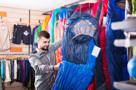 Young guy choosing new sleeping bag in sports equipment shopの写真素材