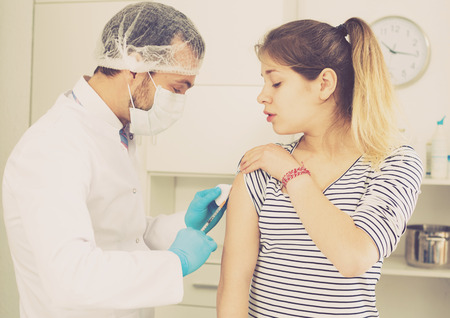Male doctor using syringe to make injection of vaccine to young patient in hospitalの写真素材