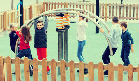 Smiling cheerful glad russian girl with long hair in school age sitting on swing on children's playground outdoorsの写真素材