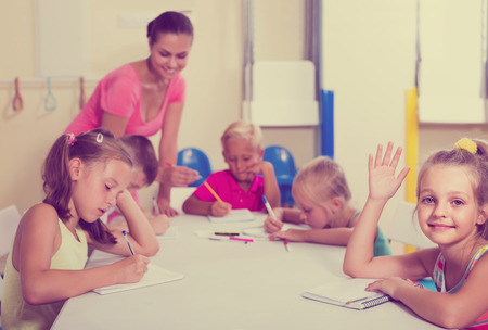 smiling children making writing exercises with help of teacher in classの写真素材